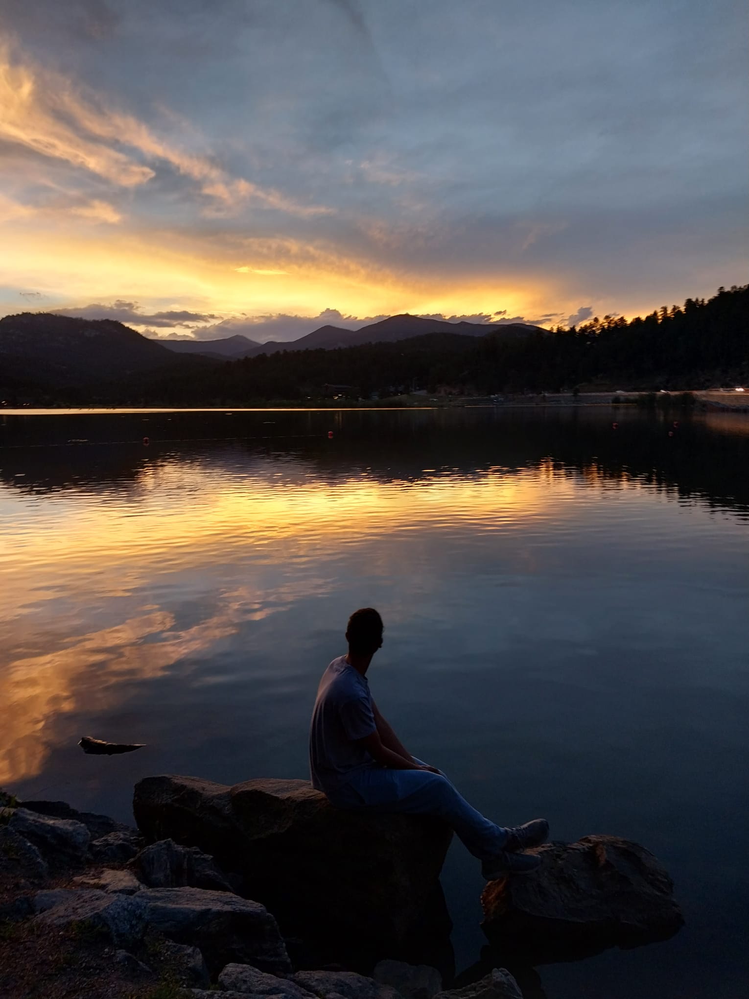 Marconi Porra sitting on a rock looking over a lake during the sunset.